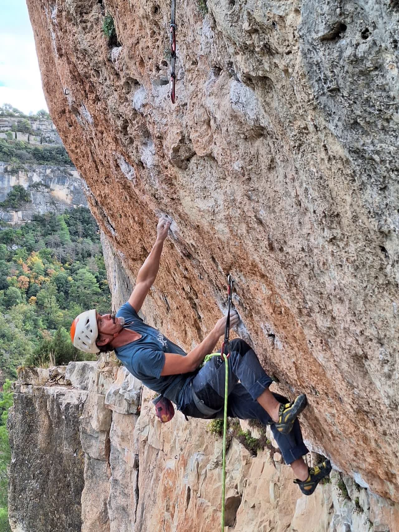 Jose escalando un techo con vistas al valle de Siurana, a punto de clipar una cinta exprés