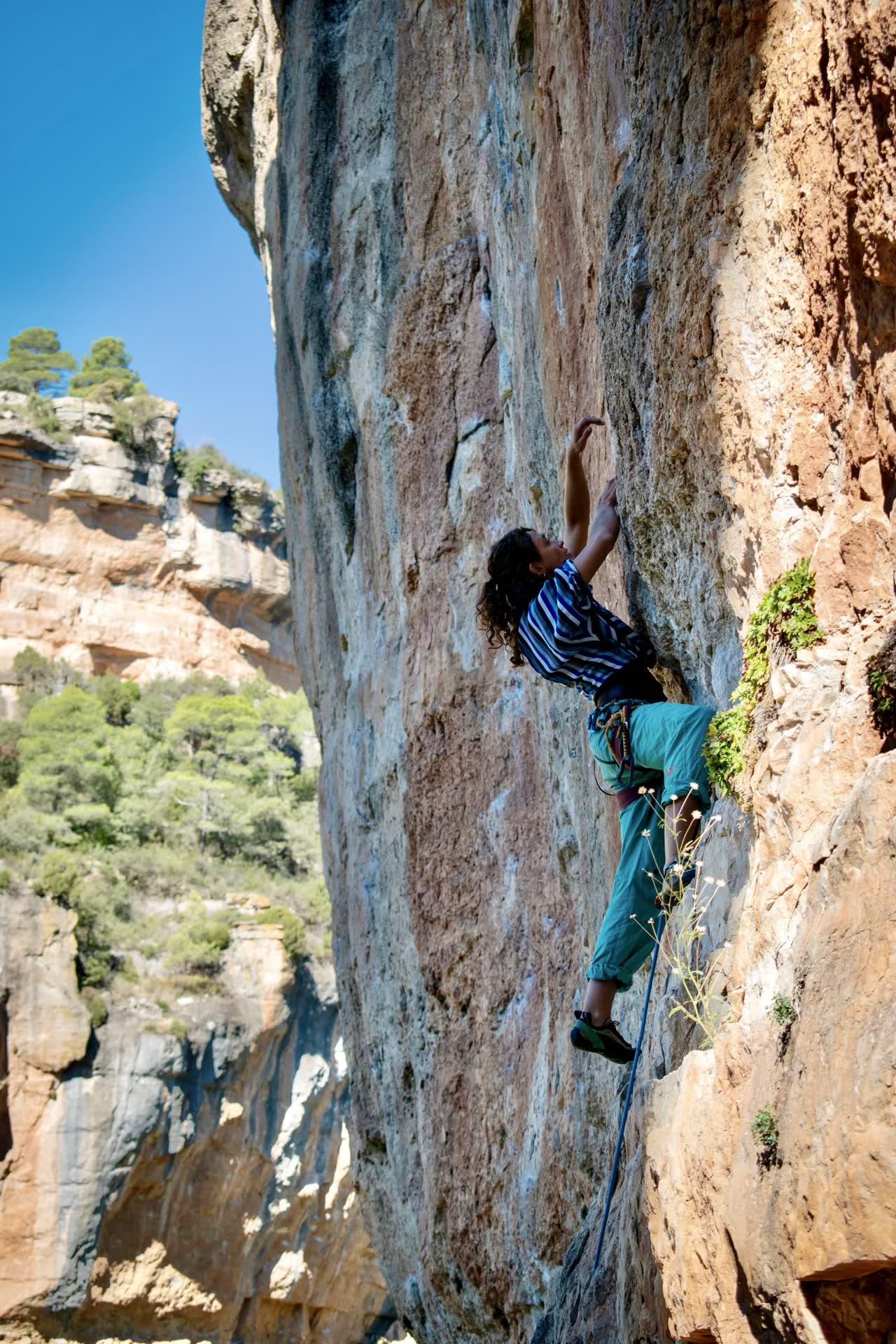Shanti escalando una pared alta en Siurana, con el valle y el cielo azul de fondo