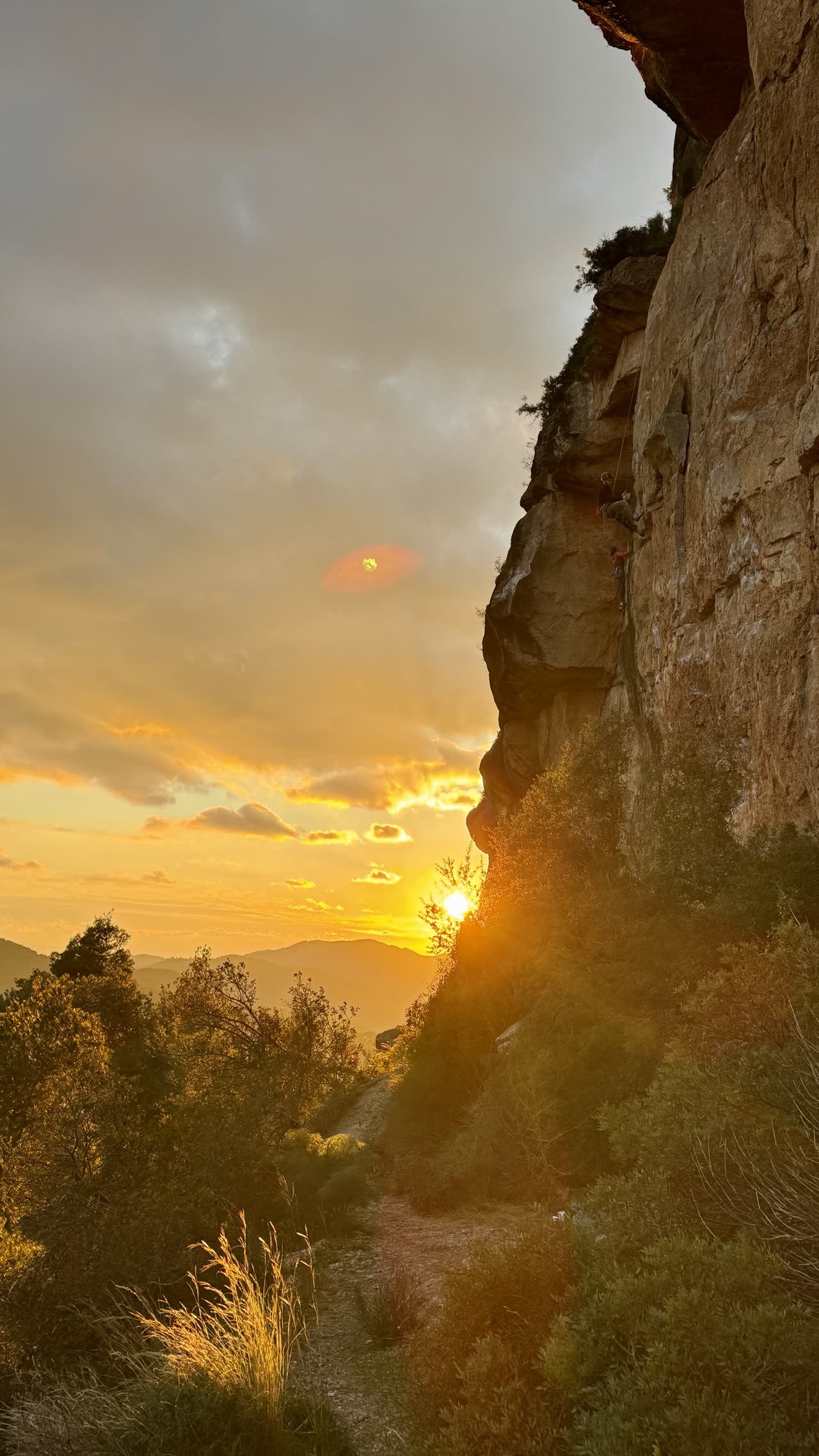 Escalador en la pared al atardecer, con el sol asomando entre los árboles