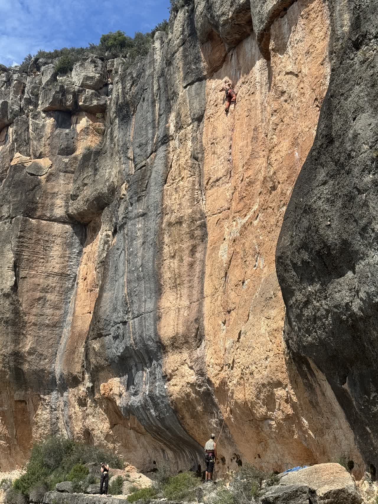 Escalador asciende una pared de roca caliza anaranjada en Siurana